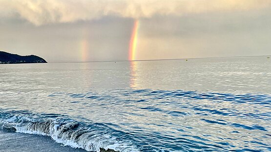 Ein Regenbogen über dem Meer an einer Sandküste