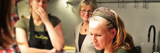 Vier Frauen stehen um einen Kochtopf herum in einer Küche