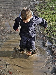 Ein kleiner Junge in Matschhose springt in eine matschige Pfütze