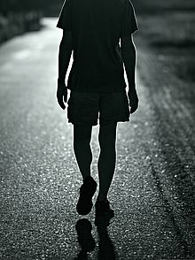 Schwarzweiß Aufnahme eines einsamen Mannes von hinten, der eine leere Straße entlangläuft